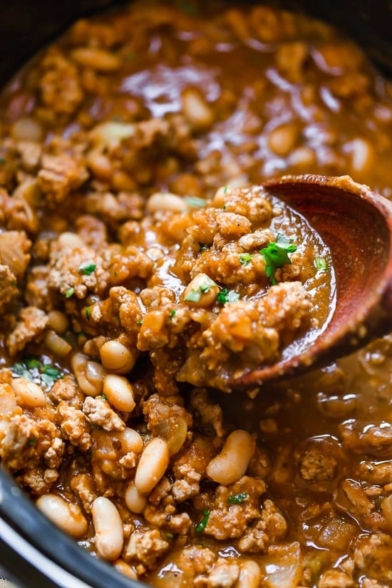 A pot of hearty chili with beans and ground meat, being stirred with a wooden spoon