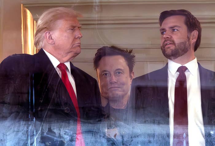 Three men stand together in discussion through a window, one in a suit with a red tie, the others in casual attire