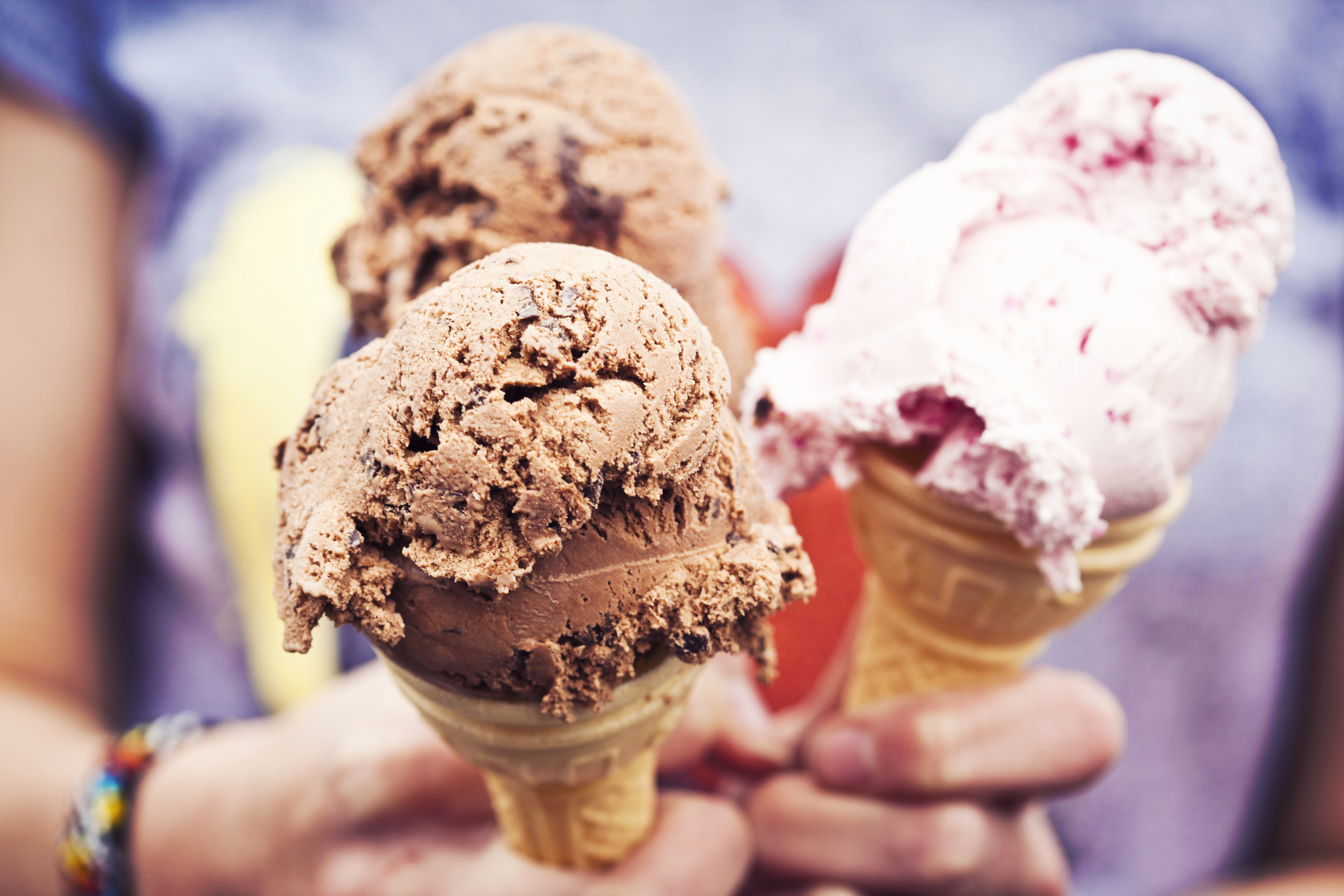 Three ice cream cones with scoops of chocolate and strawberry are held up close.