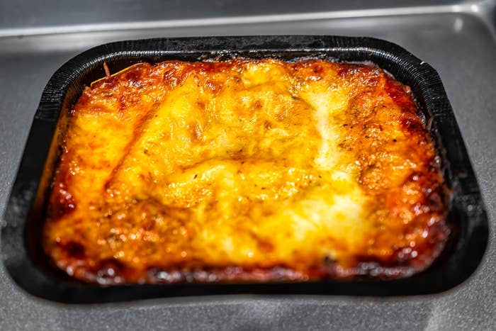 Frozen lasagna in a black tray.