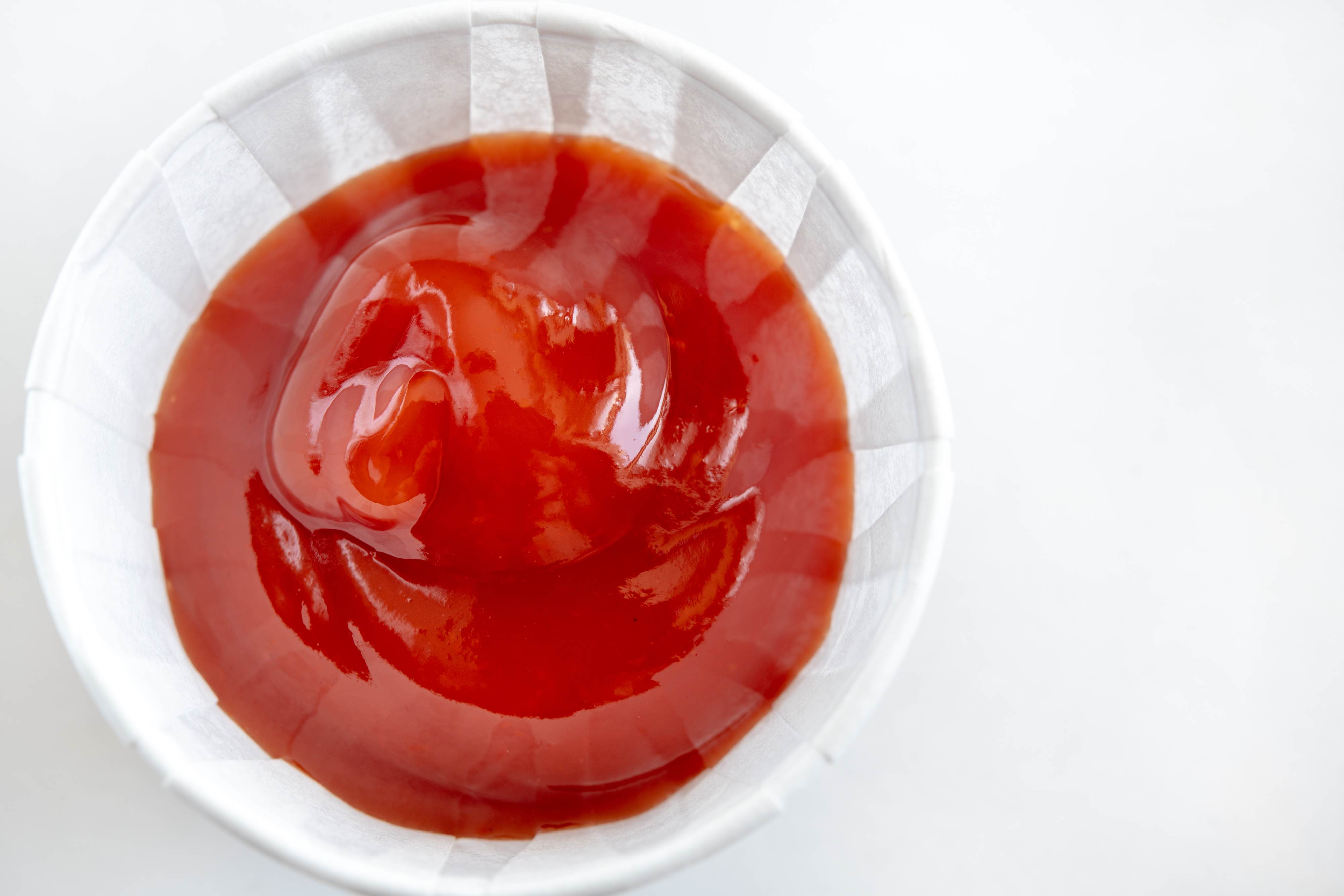 Ketchup served in a small paper cup, viewed from above.