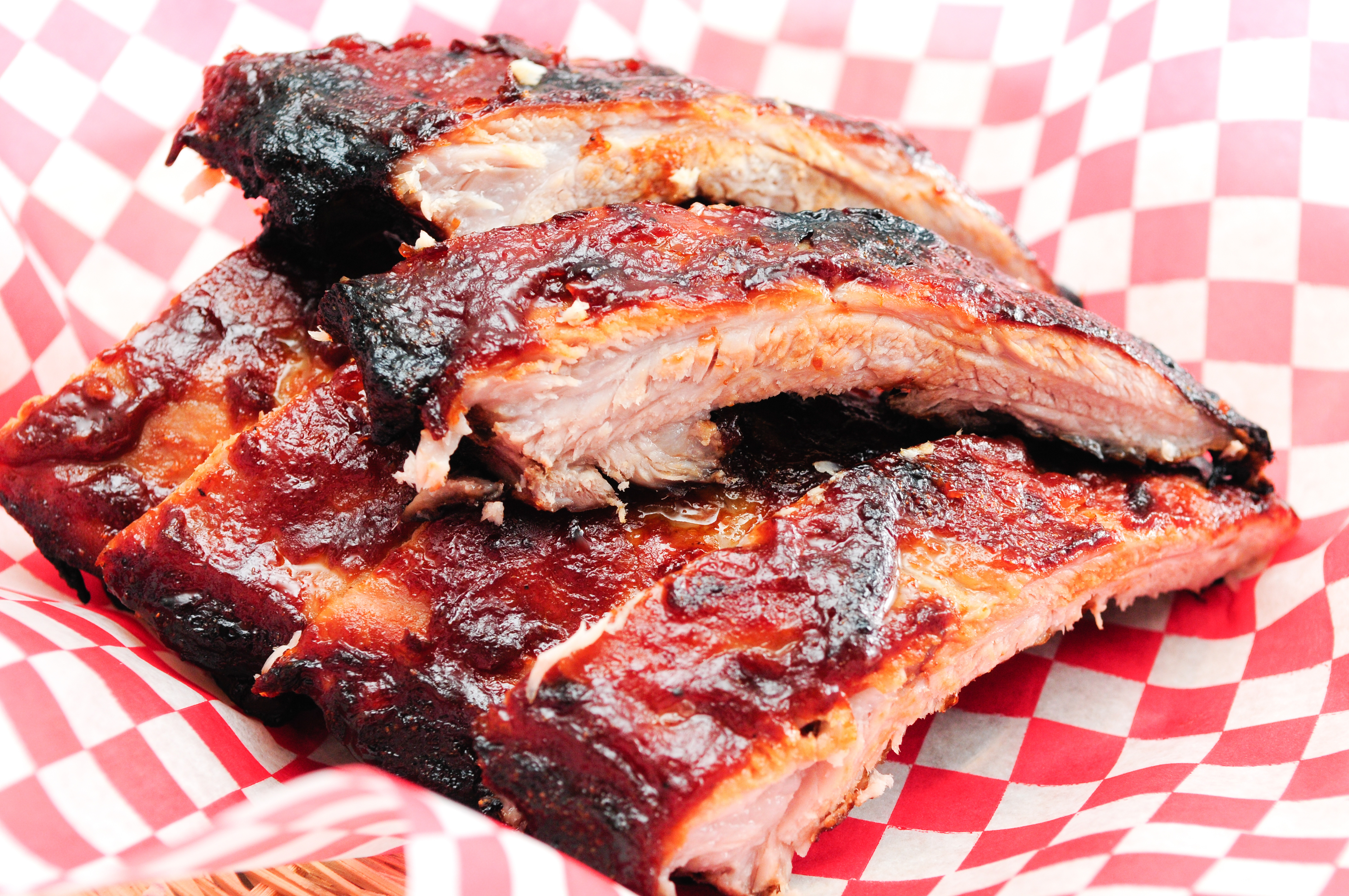 A stack of glazed barbecue ribs on a checkered paper.