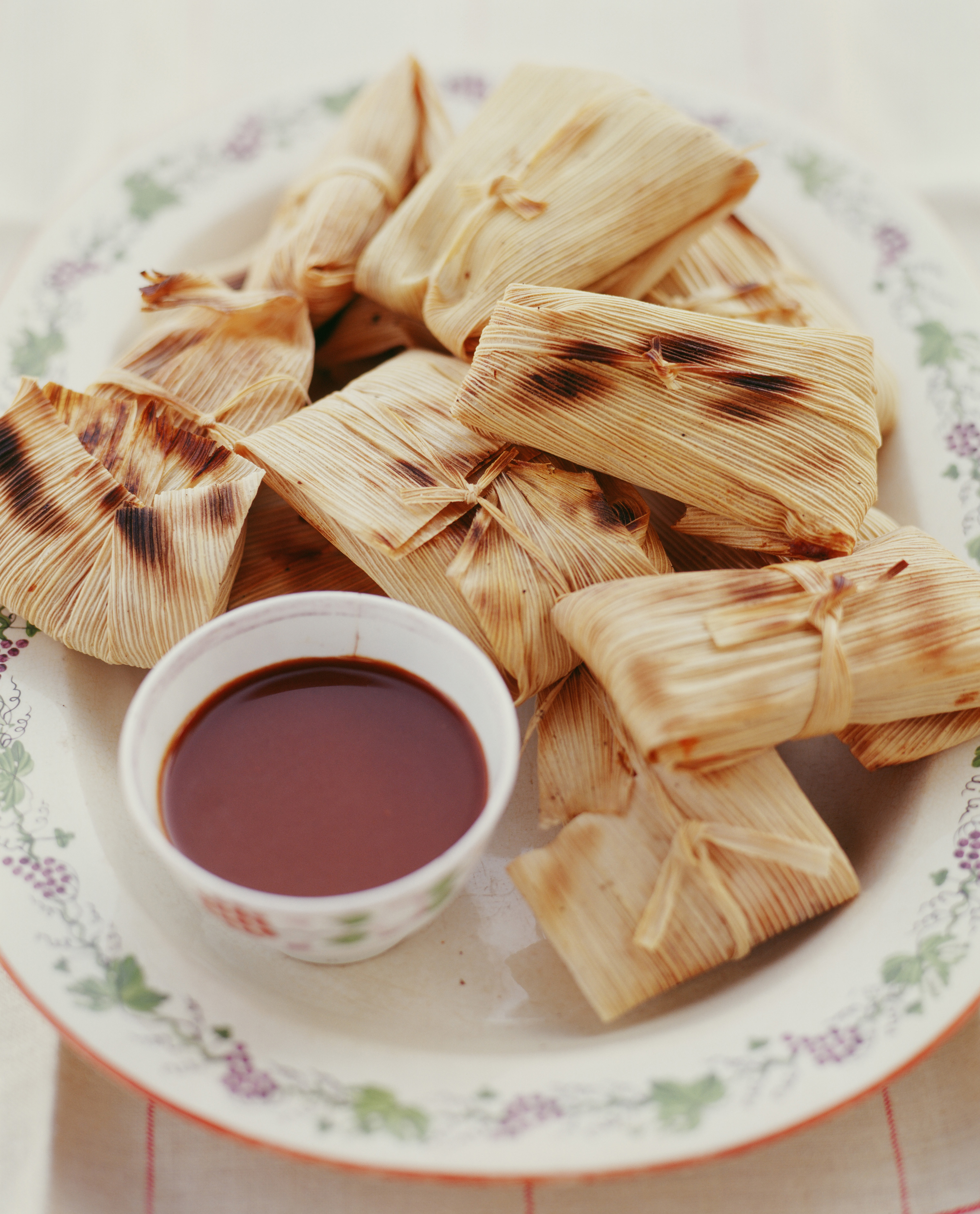 Plate of wrapped tamales with a small bowl of sauce.
