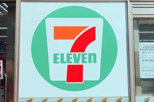 セブンイレブンの大きなロゴが窓に表示されている店舗外観。隣にポスターが貼られている。