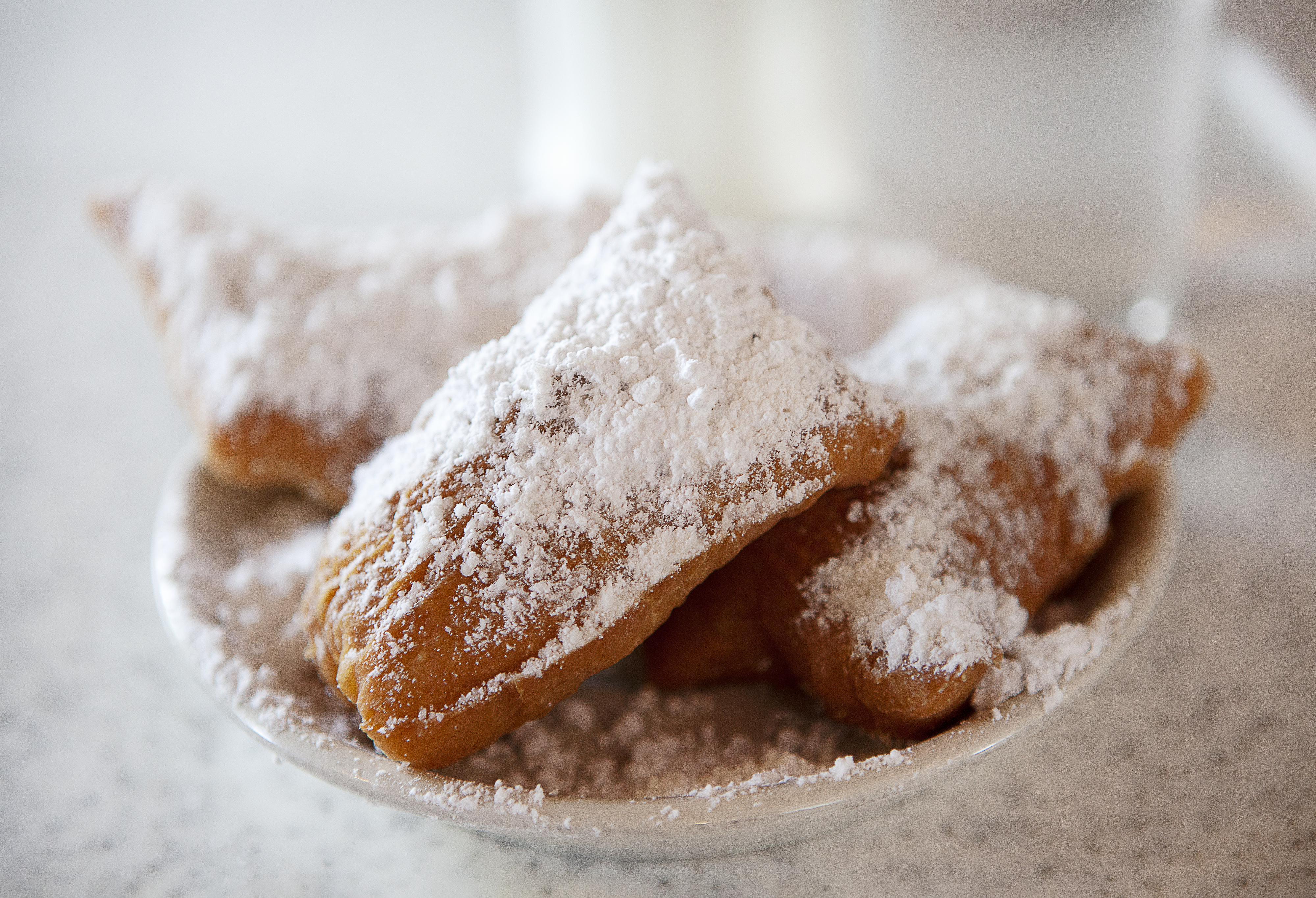 Plate of beignets dusted with powdered sugar on a table.