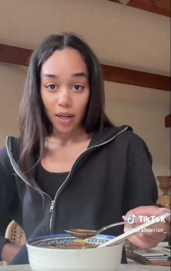 Person wearing a casual hoodie, eating from a bowl with a spoon, looks at the camera. TikTok username visible