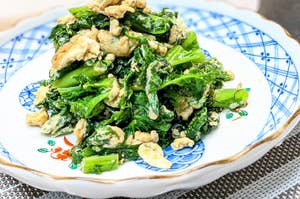 白い皿に盛られた炒めた卵と緑の葉野菜の料理。アジア風のディスプレイ。