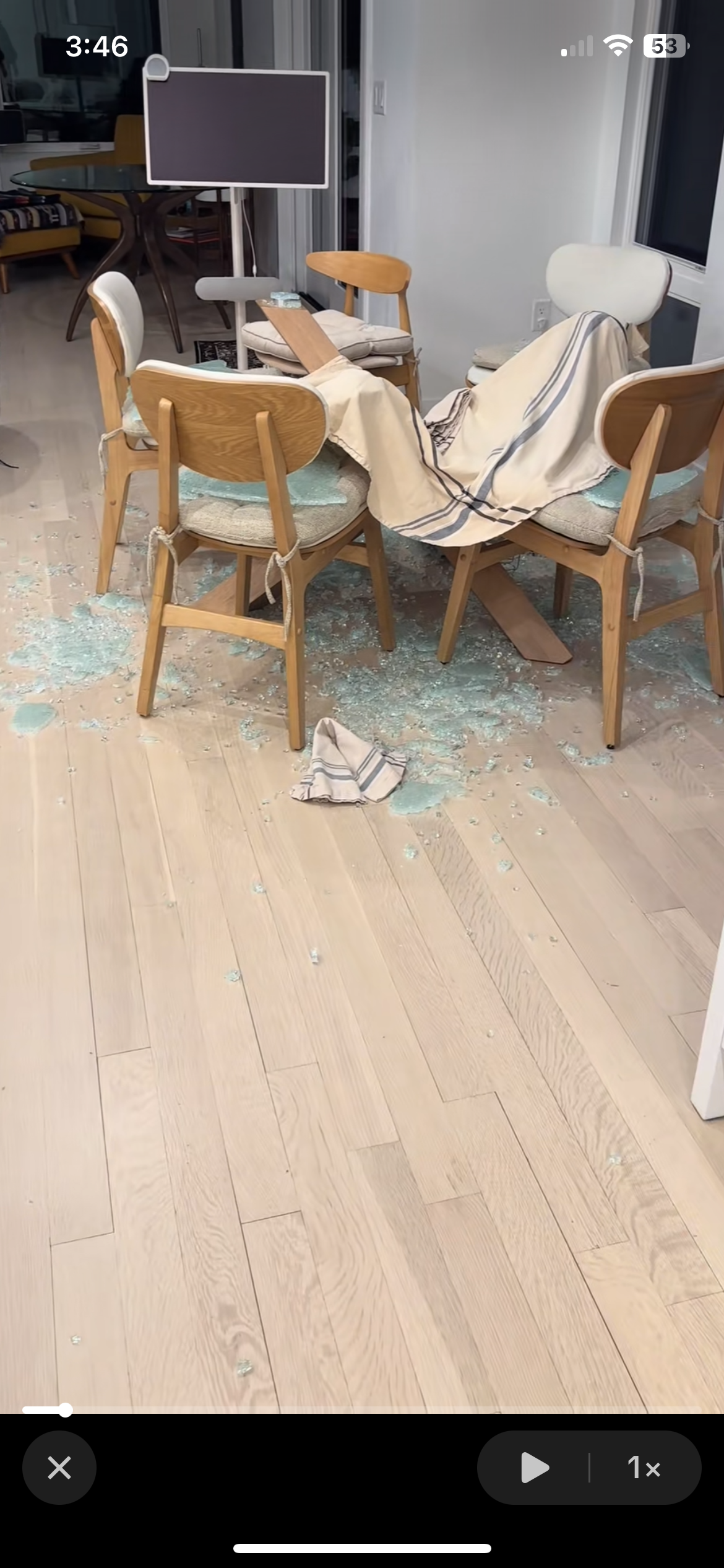 Broken glass and chairs around a dining table, with a striped cloth partially draped over them