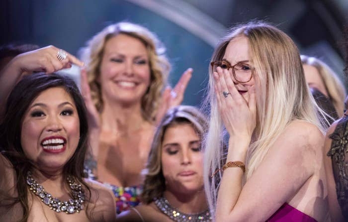 sarah hanlon, a blonde woman with glasses, holds back tears while people cheer around her
