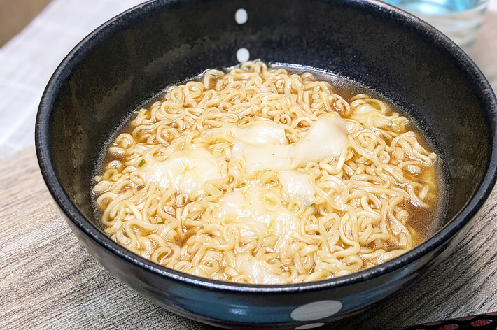 ラーメンの入った黒い器と箸。背景にガラスの水の入ったコップが見える。