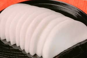 黒い皿に盛られた薄切りの大根。背景にオレンジの布がある。