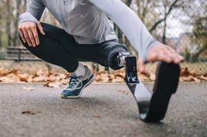 パーカーを着た男性が、屋外で人工脚を装着し、ストレッチをしています。