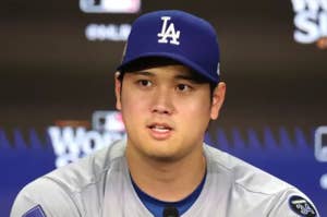 野球選手がメディア会見で公式ユニフォームを着て話している様子。背景にはロゴが表示されている。