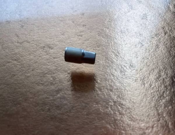 Close-up of a small metallic cylinder resting on a textured surface, casting a shadow