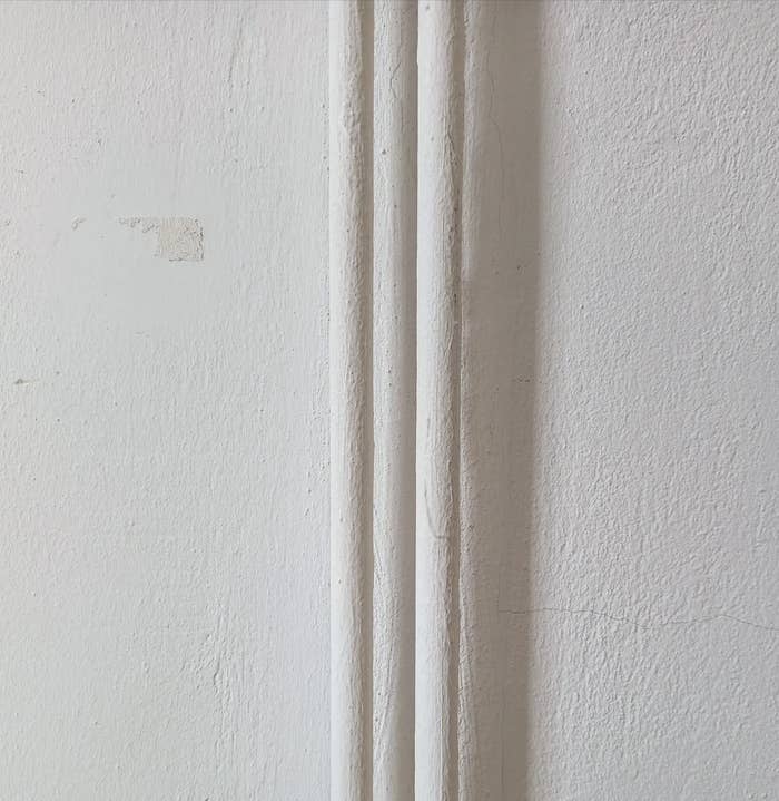 Three vertical pipes run along a textured white wall