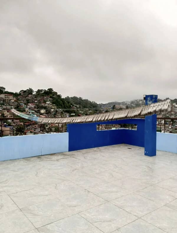 Rooftop with curved, weathered structure overlooking hillside neighborhood under cloudy sky
