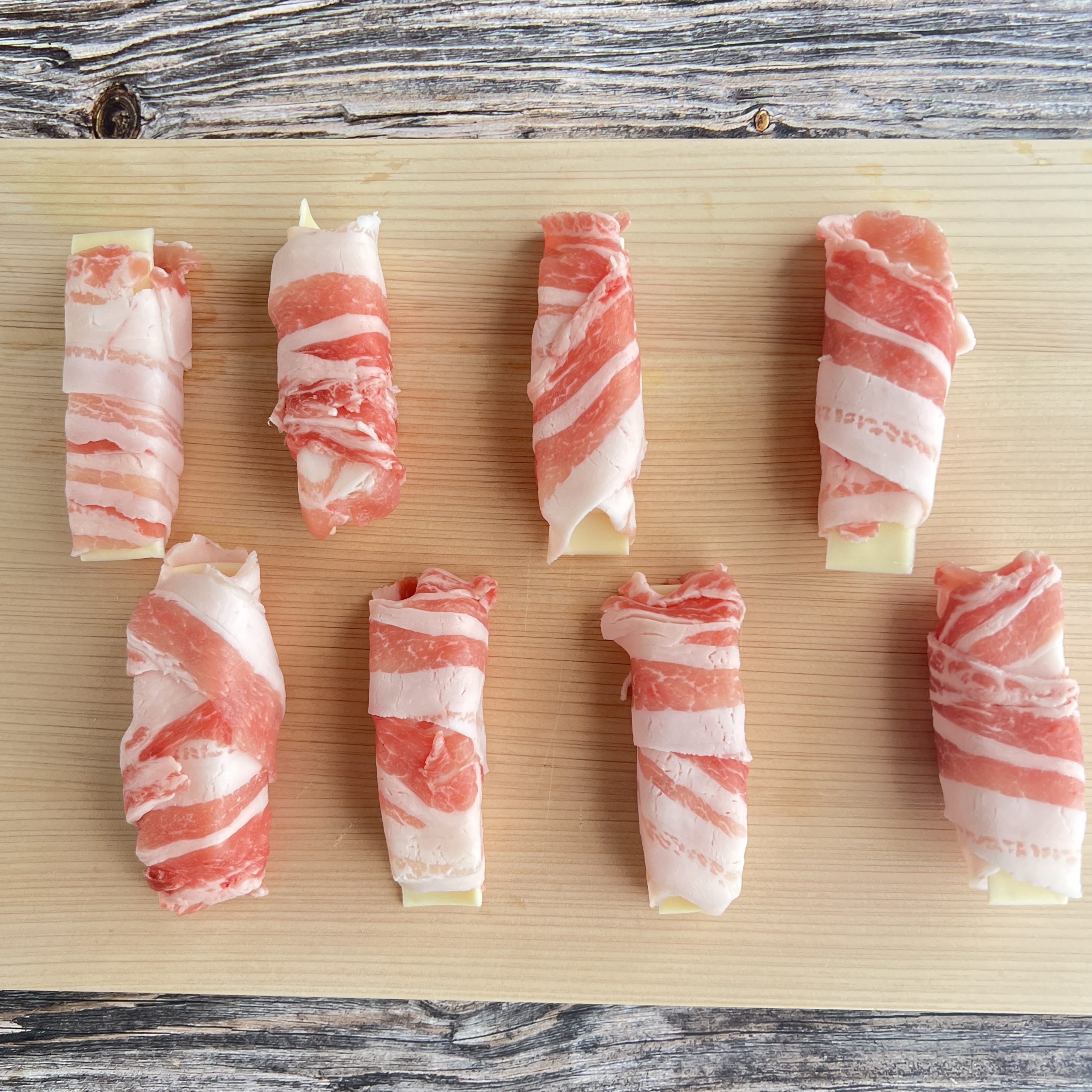 木製まな板の上に置かれた、巻かれた豚肉が並んでいる。