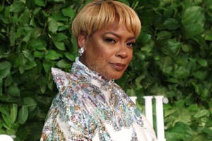 Celebrity in elegant floral-patterned dress at an event, posing against a leafy backdrop