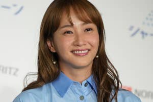 女性がカメラに向かって微笑んでいる。爽やかな雰囲気の青いシャツを着用。バックはイベントのロゴ。