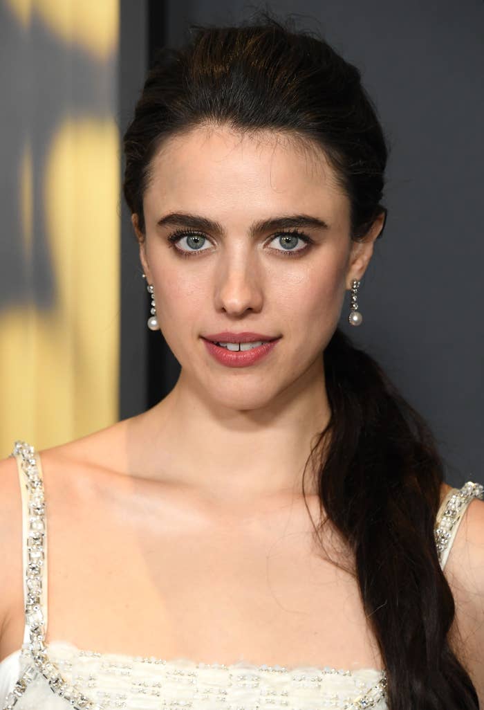 Margaret Qualley with long dark hair wearing a beaded top and pearl earrings, looking directly at the camera