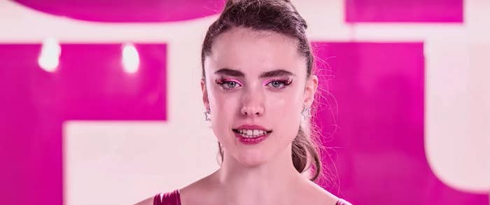 Margaret Qualley with styled hair and sparkly eye makeup looks forward, standing against a bold background with large text partially visible