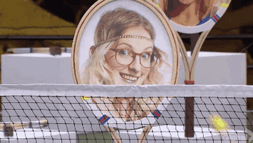 Tennis racquet with a smiling woman&#x27;s face on the strings, displayed behind a tennis net