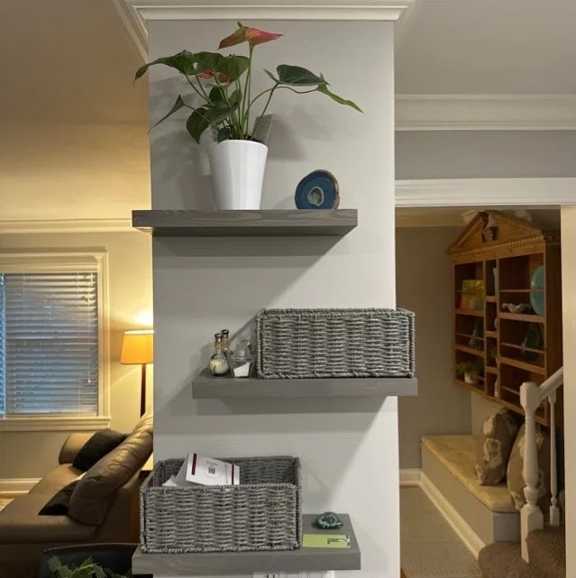 Three decorative shelves with a potted plant, geode, and wicker baskets holding items, placed in a cozy living room setting with a lamp and staircase