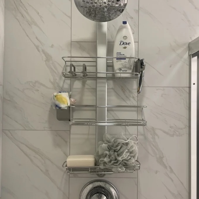 Shower caddy with Dove body wash, a loofah, soap bar, and various toiletries, set in a marble-tiled bathroom shower