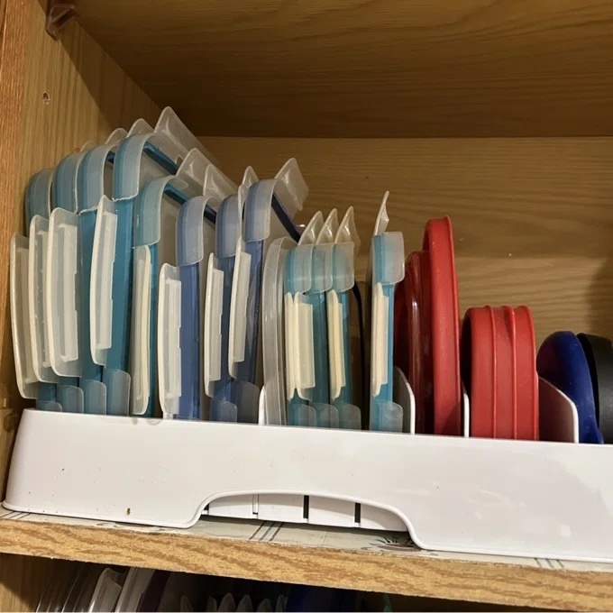 Organized cabinet shelf with cutting boards and lids in a white holder, showcasing tidy kitchen storage solutions