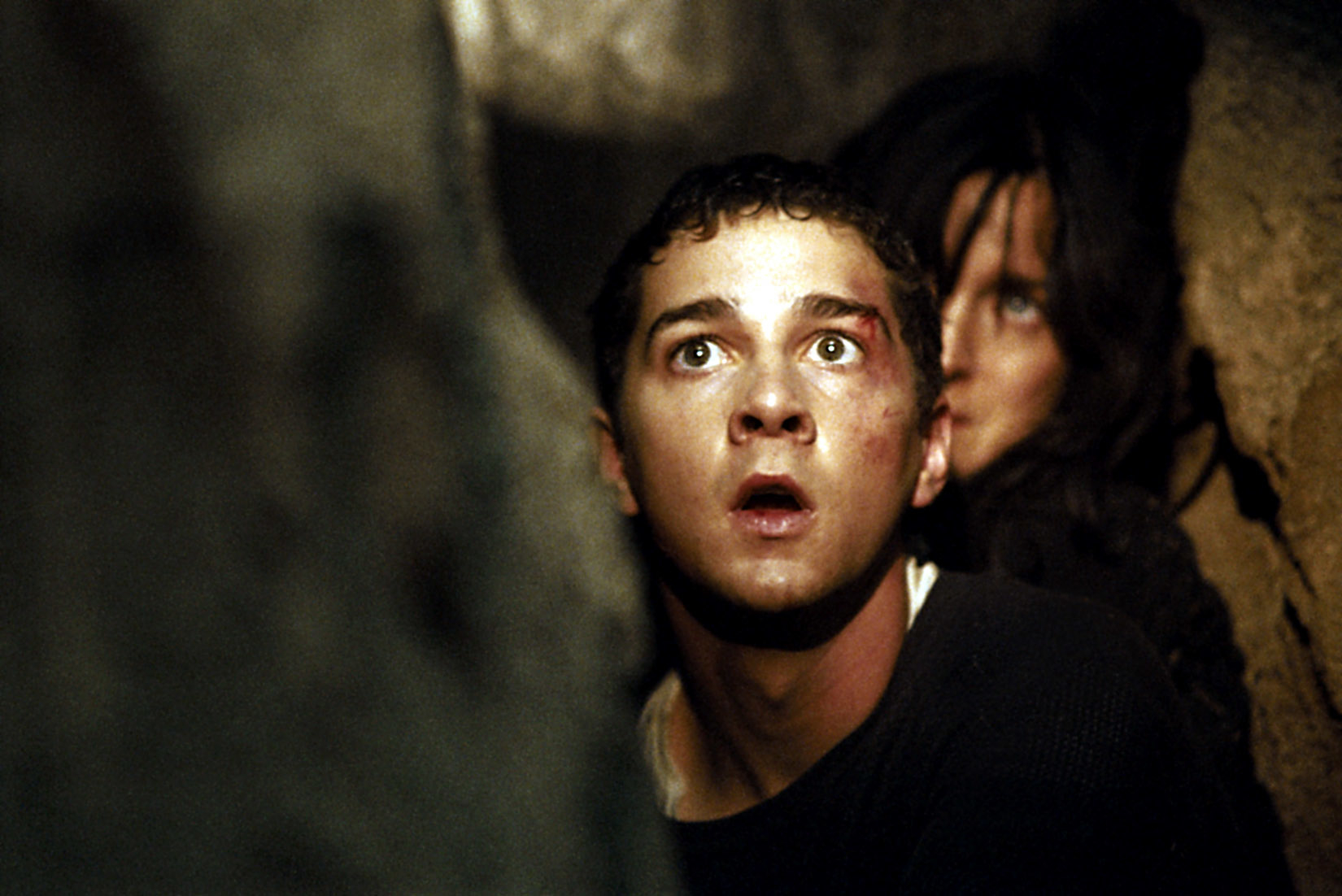 Two people in a cave with a shocked expression, dim lighting highlights their faces. Context suggests a suspenseful or dramatic scene