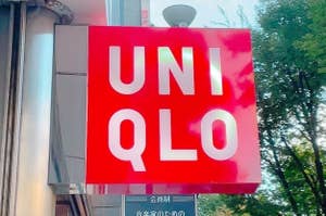 A vertical sign outside a store displays the brand name "Uniqlo" in bold white letters on a red background. Trees are visible in the background
