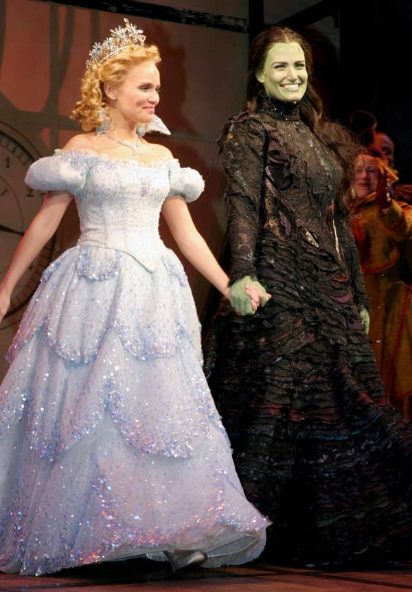 Kristin and Idina on stage: Kristin in a sparkling ball gown and crown, and Idina in an elaborate, dark outfit with green makeup