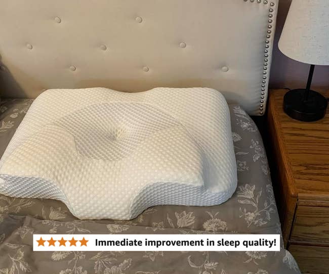 Ergonomic pillow on a decorated bed near a nightstand with a lamp, showcasing bedroom essentials for comfort and support