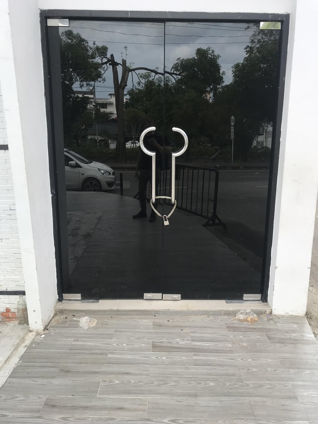 Glass door with a handle shaped like a stylized male genitalia, reflecting the street scene outside