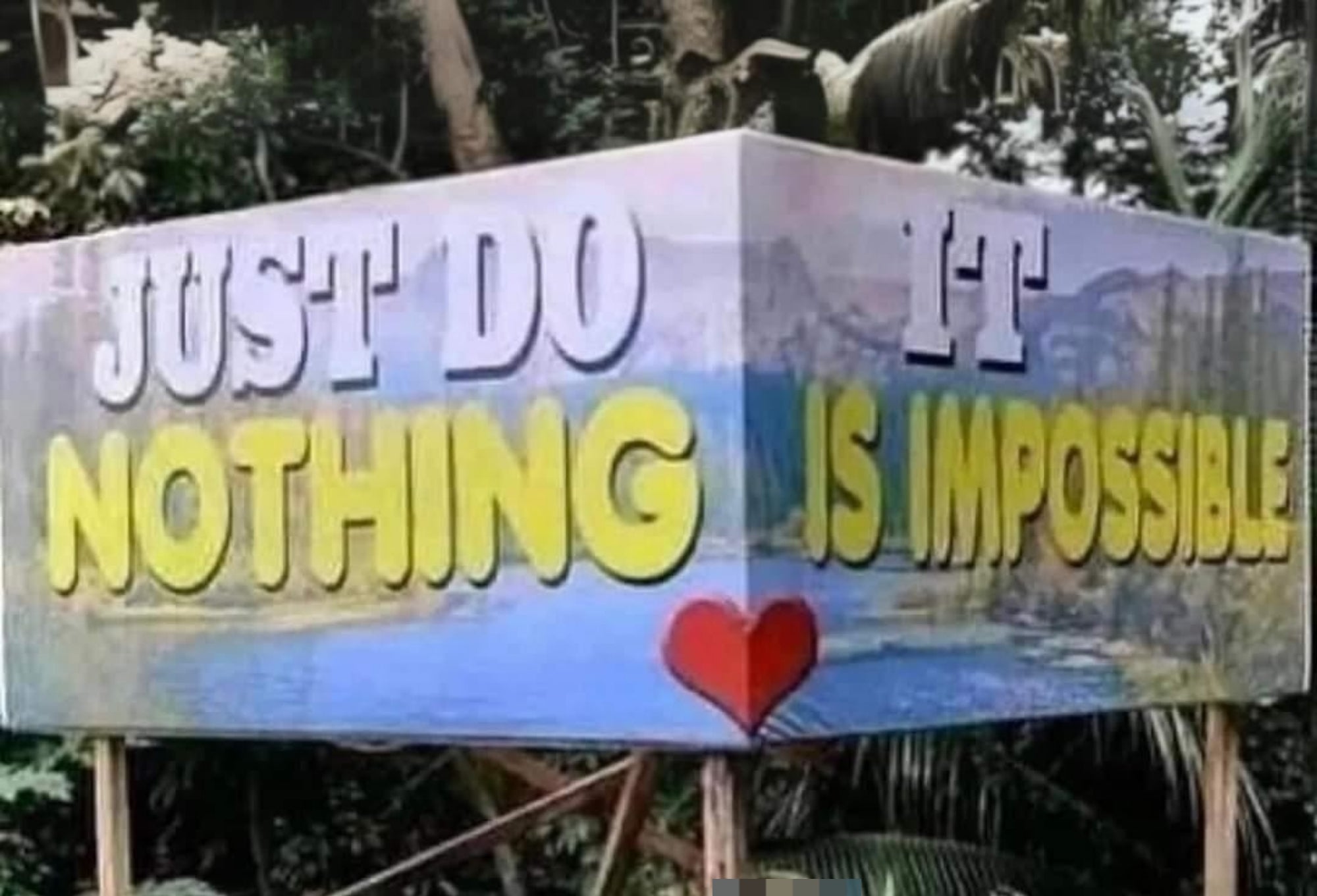 Person crouching and smiling in front of a humorous sign that reads "Just Do Nothing. It is Impossible" with a heart between the phrases