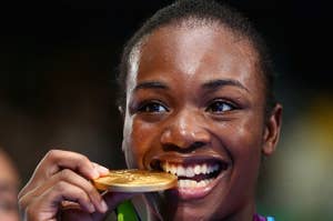 Person holding a gold medal, smiling while gently biting it. Wearing sports attire, likely from a sporting event