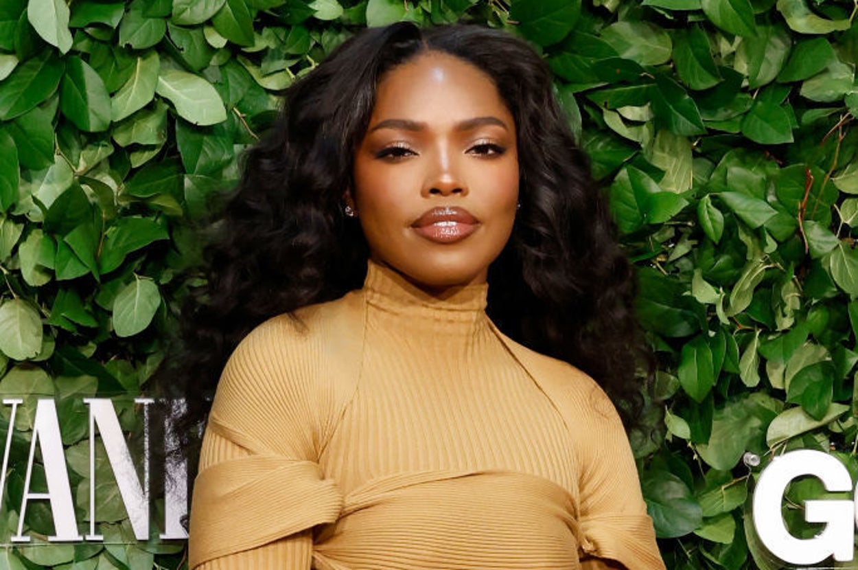 Person in a stylish, form-fitting dress poses in front of a leafy backdrop at a celebrity event