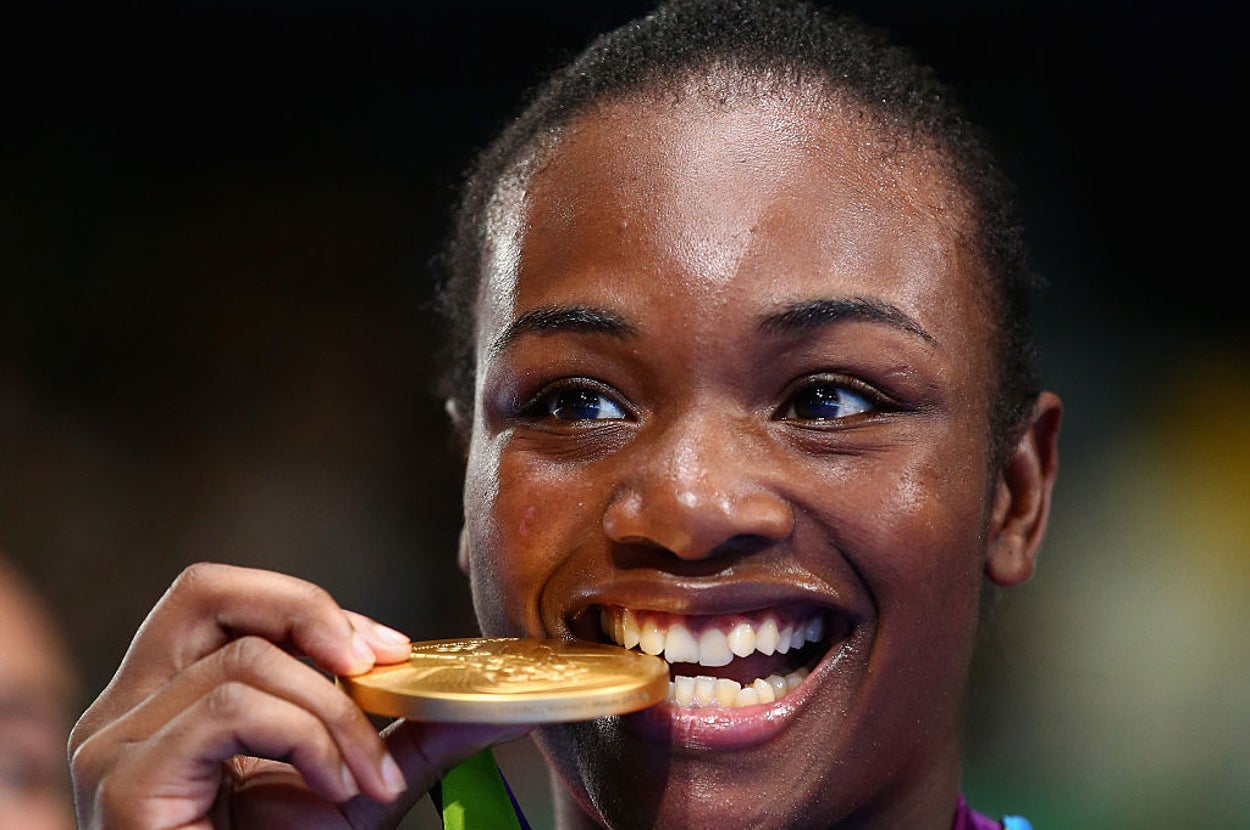 Person holding a gold medal, smiling while gently biting it. Wearing sports attire, likely from a sporting event