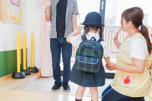 母親が幼稚園の制服を着た子どもを家の玄関で見送っている場面。