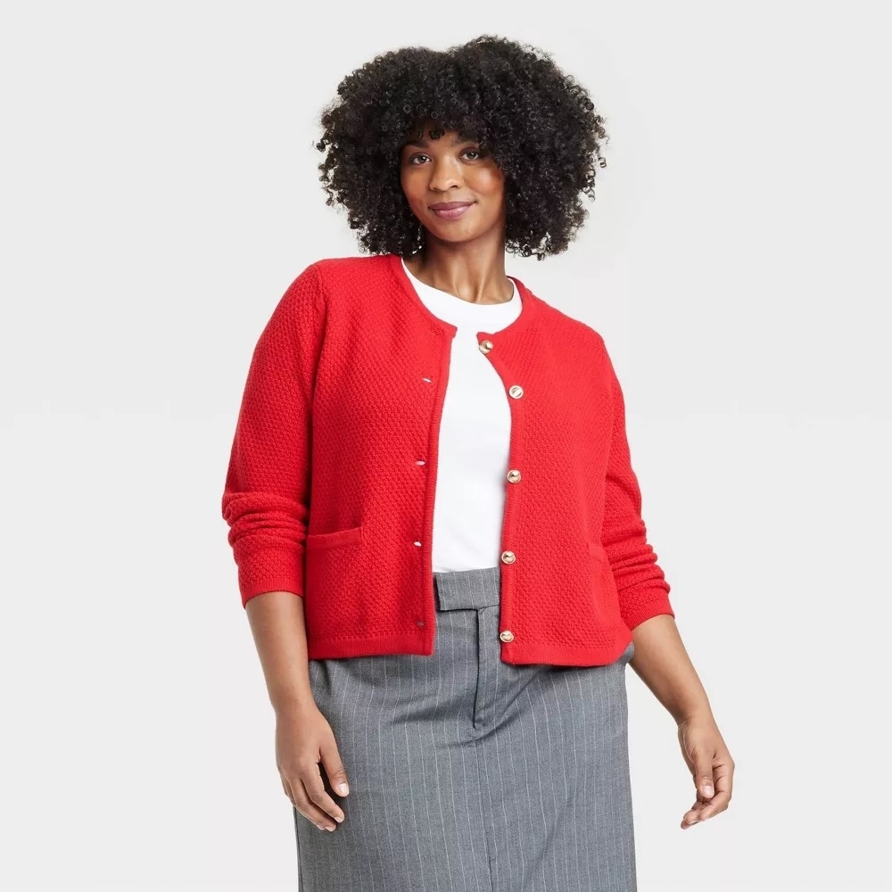 Person wearing a textured cardigan over a white top and gray skirt, posing for a fashion-related shopping article