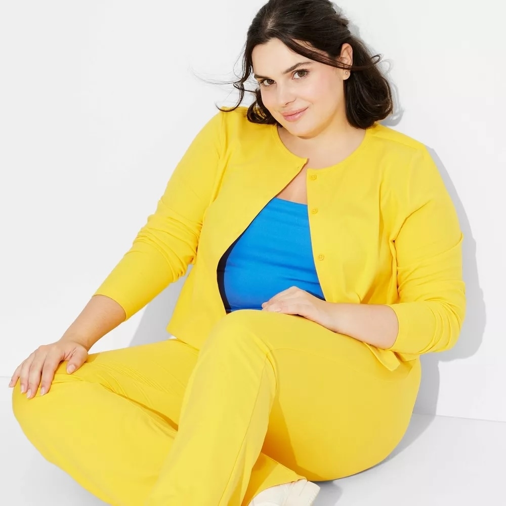 Woman in bright outfit sits casually; wears a matching top and pants with a contrasting underlayer. Fashionable and relaxed pose for a shopping article