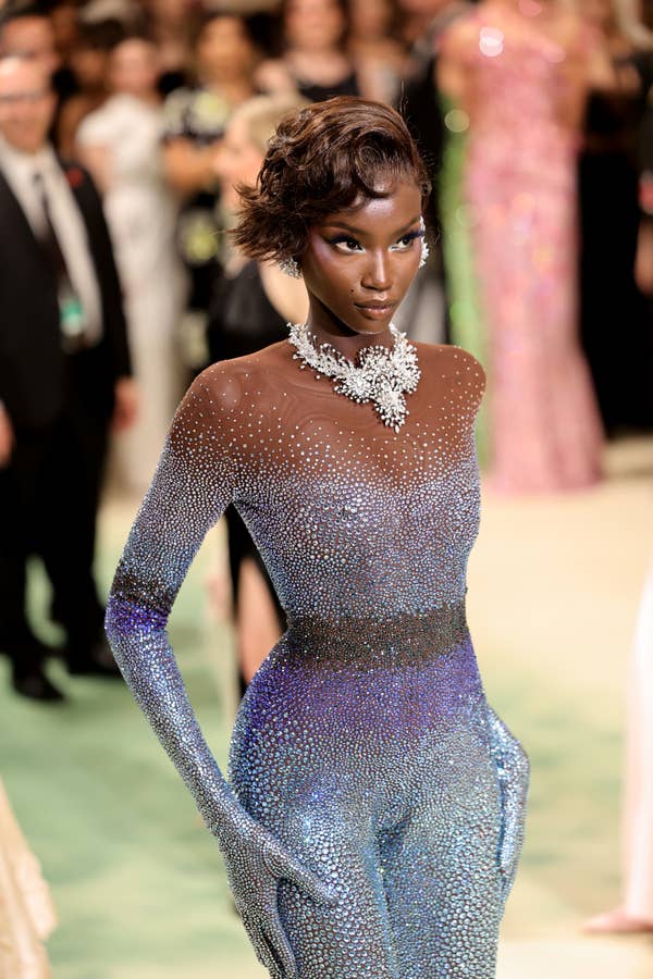 Anok Yai at the Met Gala wearing an intricately detailed, shimmering full-body outfit with a large, ornate necklace