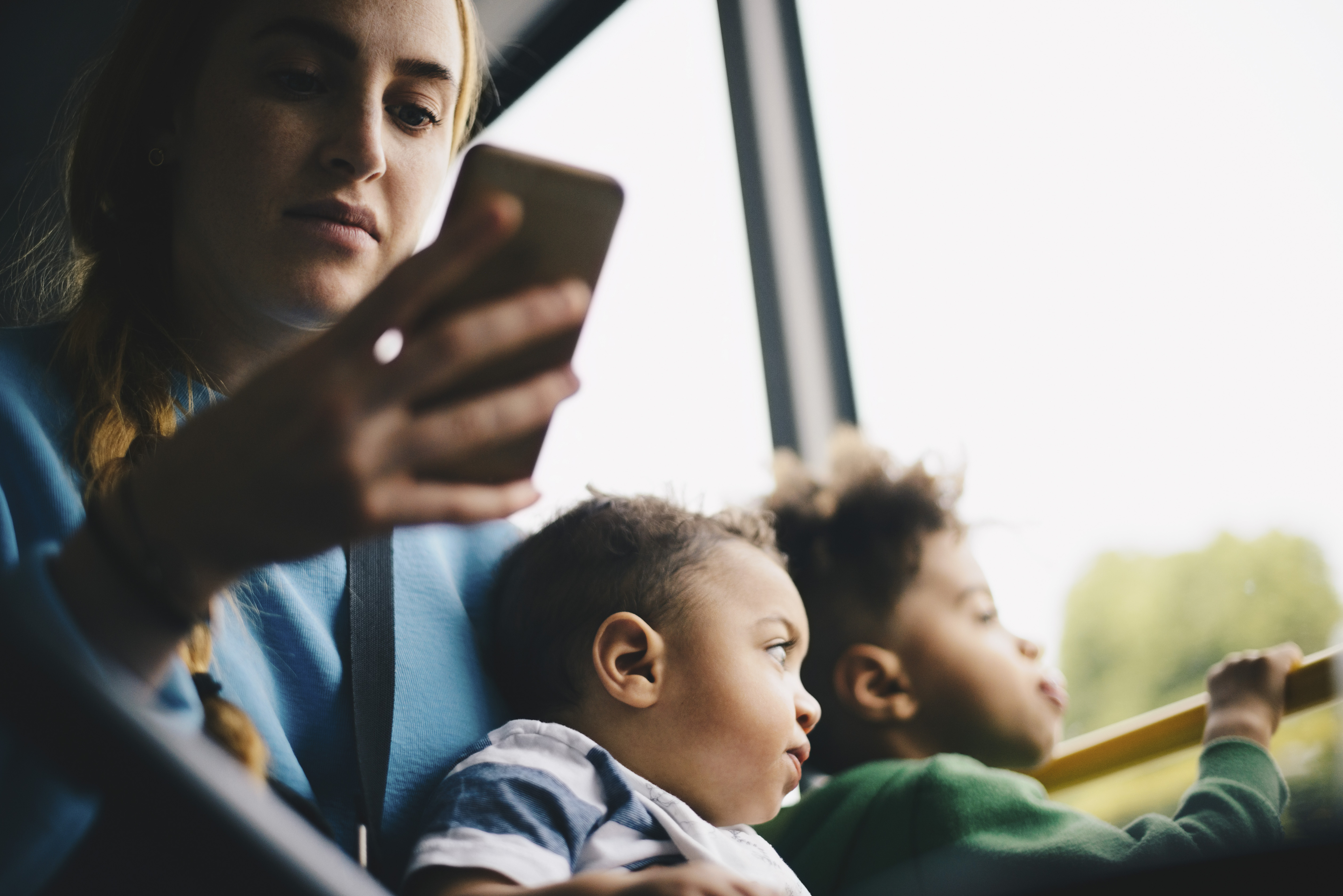 Person on a bus with two children looking out the window, while holding a smartphone