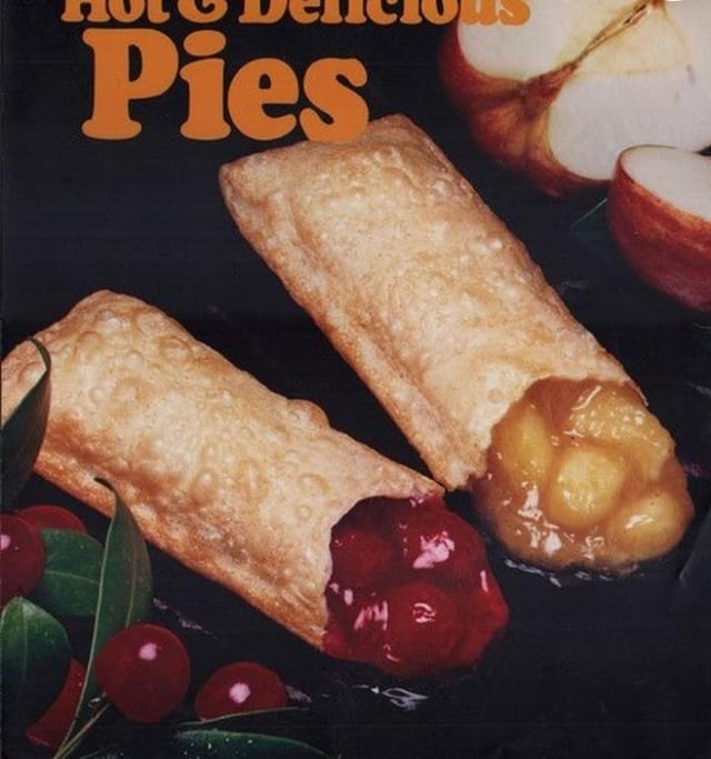 Vintage advertisement showing 2 pastries filled with cherry and apple, surrounded by fruit. Text reads "Hot & Delicious Pies."