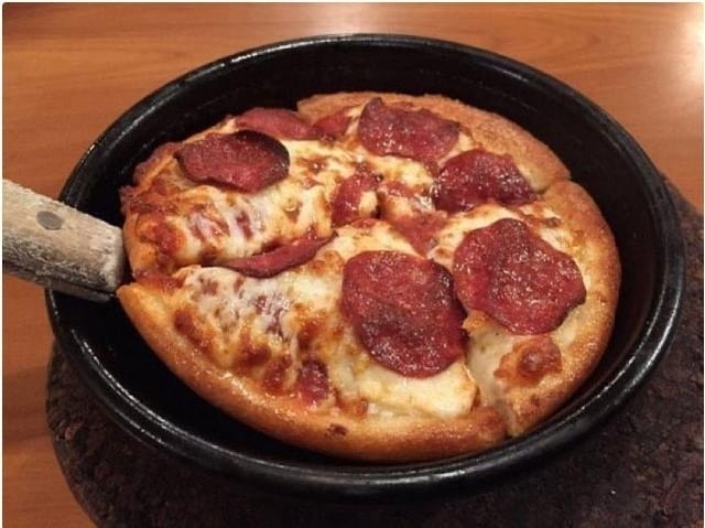 Deep-dish pepperoni pizza successful a achromatic pan, resting connected a woody table