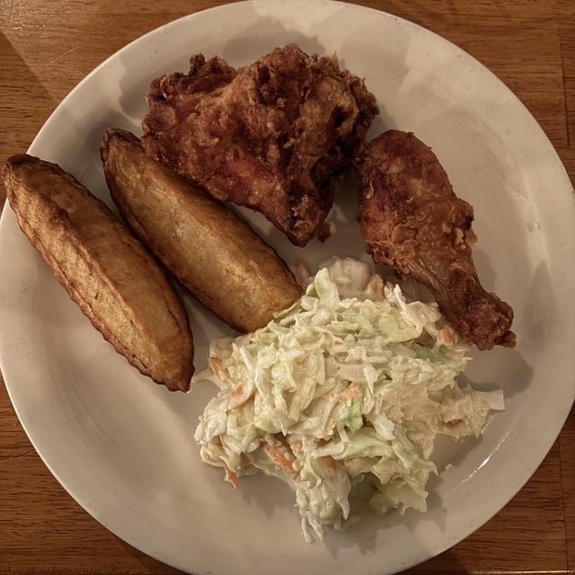 Plate with fried chicken, murphy wedges, and coleslaw connected a woody table