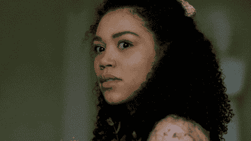 Person with curly hair turns and looks surprised, holding a plant