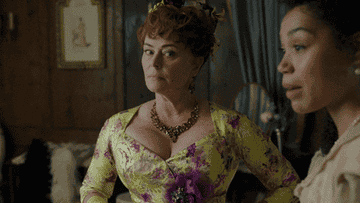 Two women in 19th-century period costumes, one with an elaborate updo and necklace, glancing sideways in a historical setting