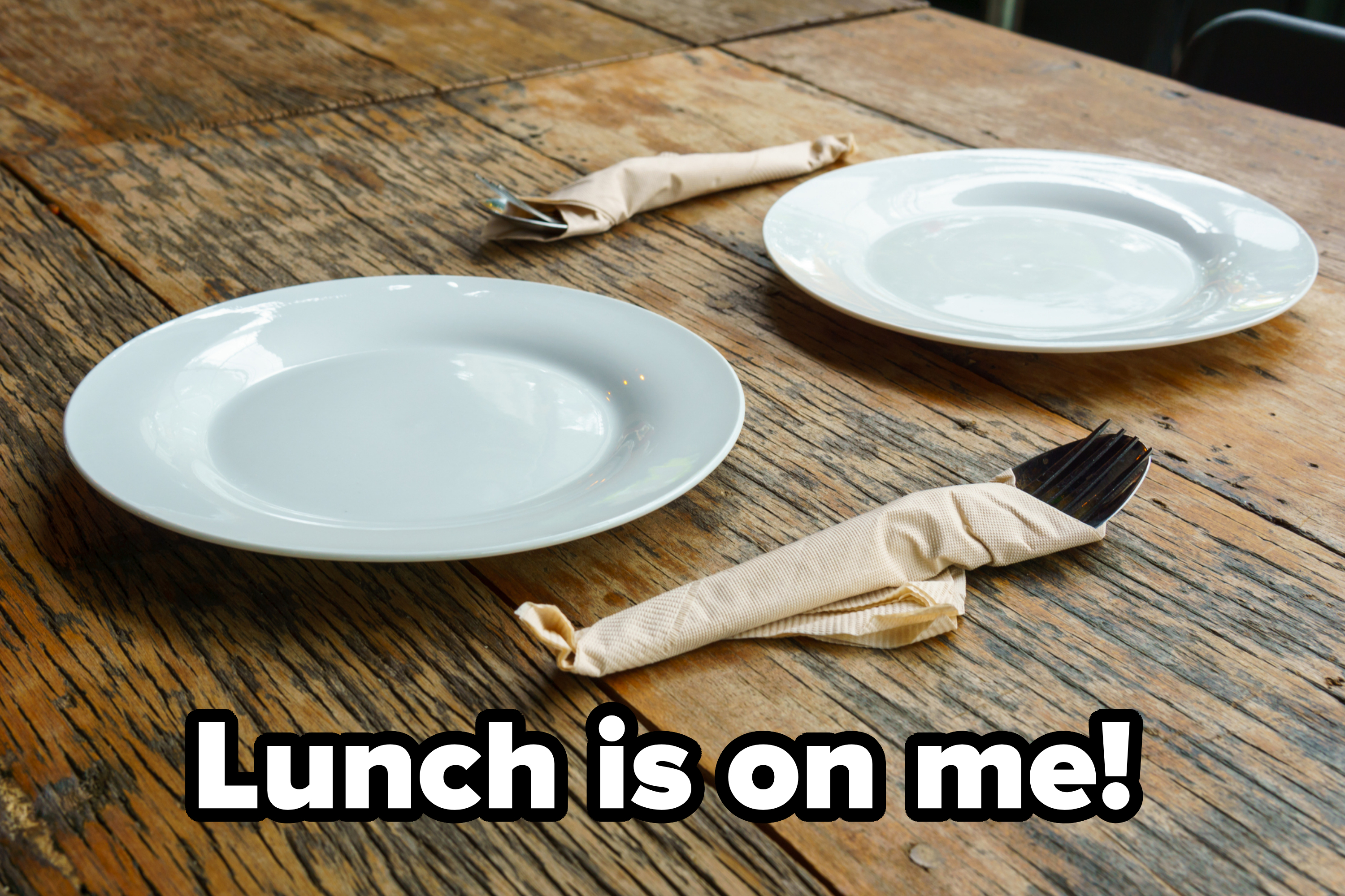 Two empty white plates on a rustic wooden table with forks and knives wrapped in napkins beside them