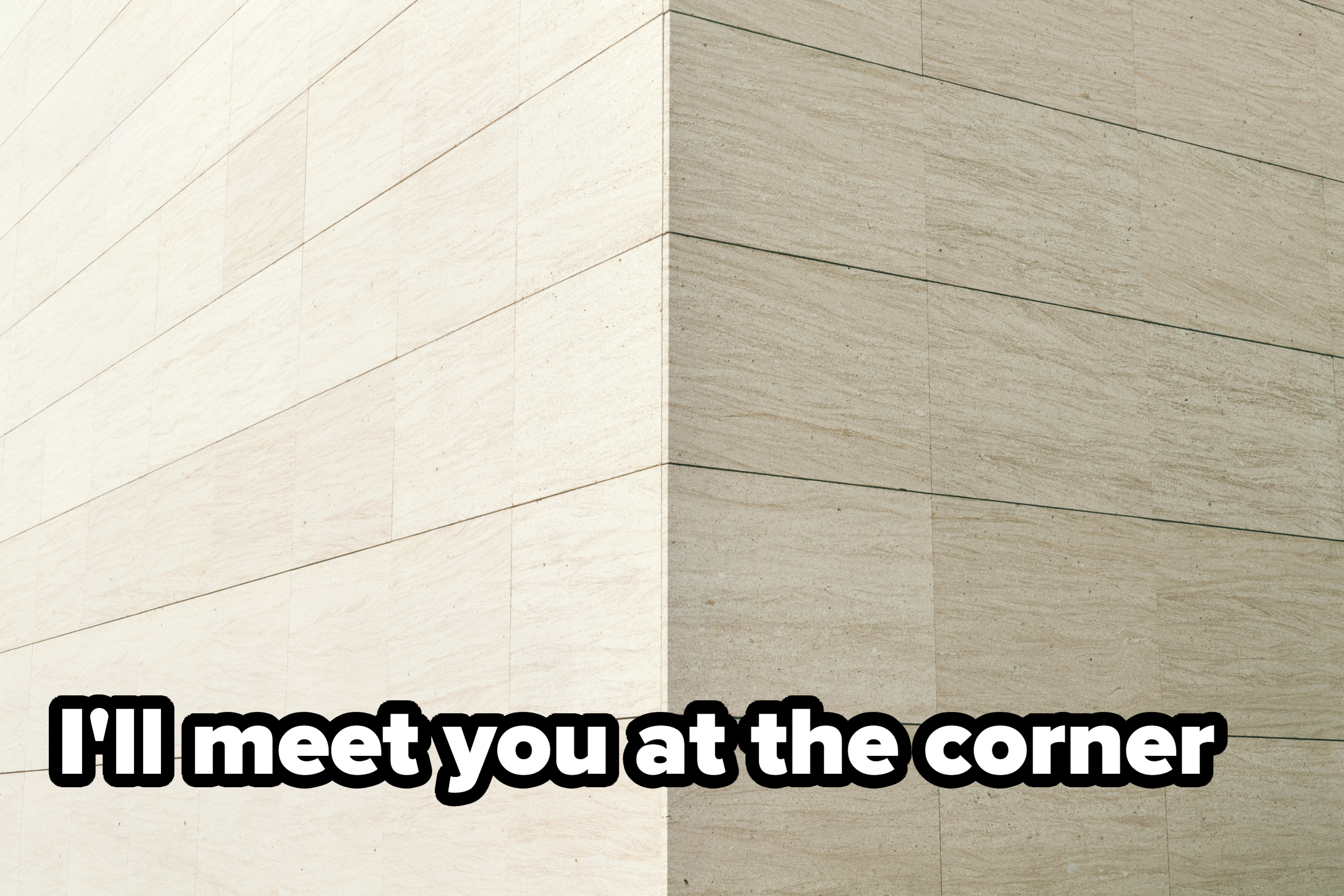 Corner angle view of a large, modern building with light stone tile walls, showcasing minimalist architecture